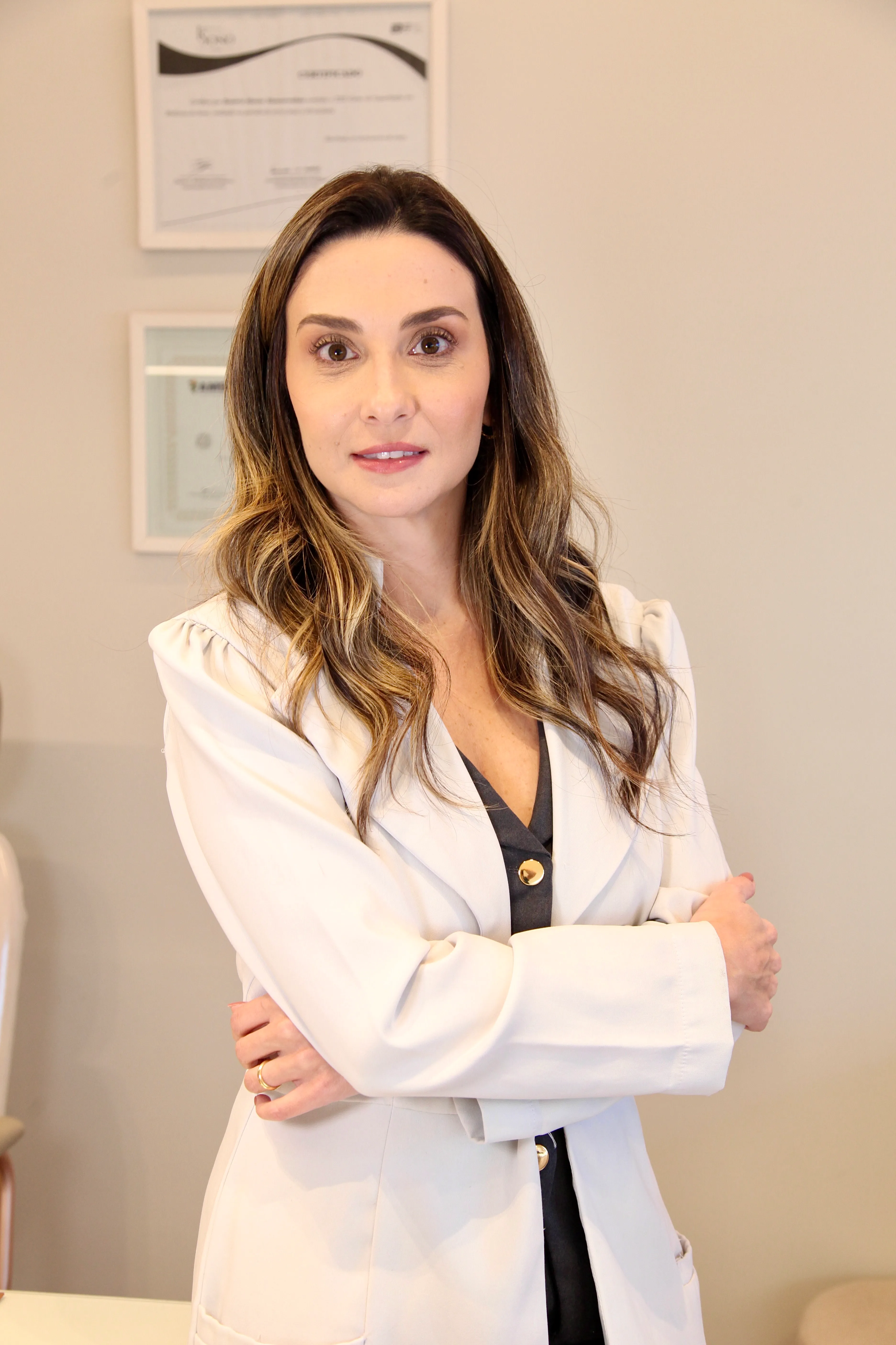 Dra. Juliana Orsini de jaleco, com seus diplomas ao fundo